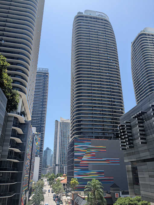 A tall building with a colorful pattern on its side stands in front of other buildings.