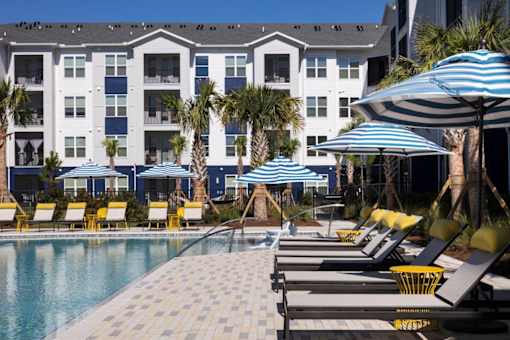 A pool area with sun loungers and umbrellas in front of a white building.