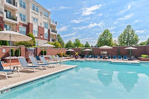 A pool surrounded by chairs and umbrellas in front of a building.