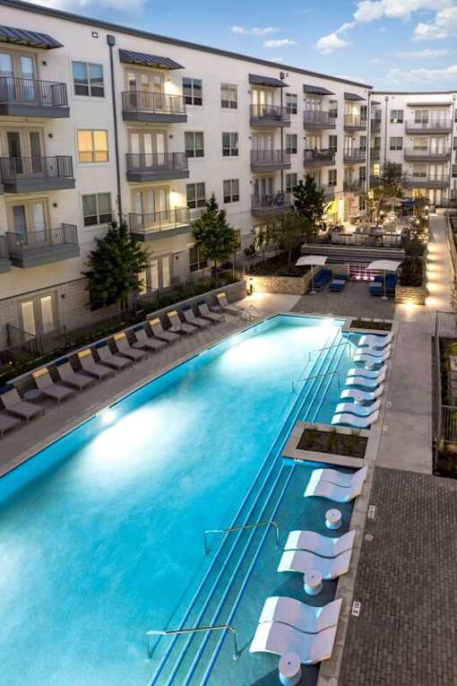 A swimming pool surrounded by lounge chairs in front of apartment buildings.