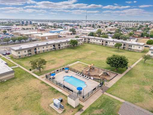 A large grassy area with a pool and apartment buildings in the background.