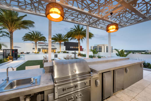 the outdoor kitchen has stainless steel appliances and a view of the pool and palm trees