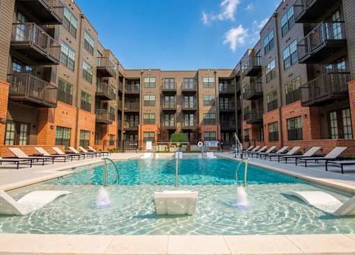 A swimming pool in front of apartment buildings with fountains in the middle.