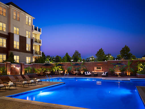 A swimming pool surrounded by lounge chairs and umbrellas at dusk.