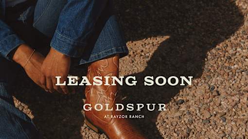 A person is sitting on the ground with their legs crossed, wearing blue jeans and brown boots.