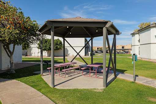 A picnic shelter with a table and benches is situated in a grassy area.