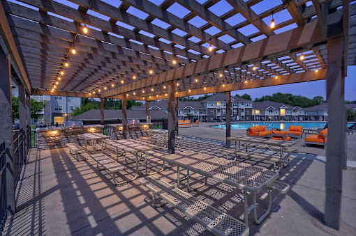 A wooden pergola with lights is over a pool area.