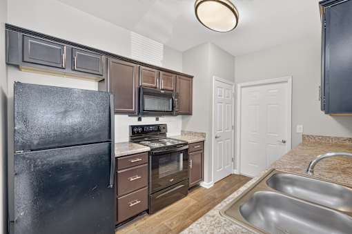 A kitchen with a black refrigerator, brown cabinets, and a stainless steel sink.