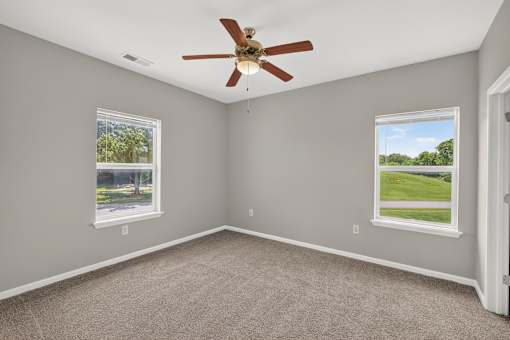 A room with a ceiling fan and two windows.