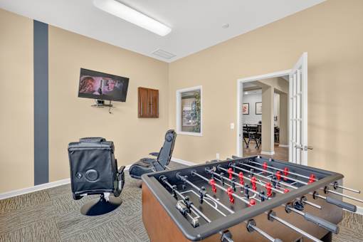 A foosball table is in the middle of a room with a television mounted on the wall.