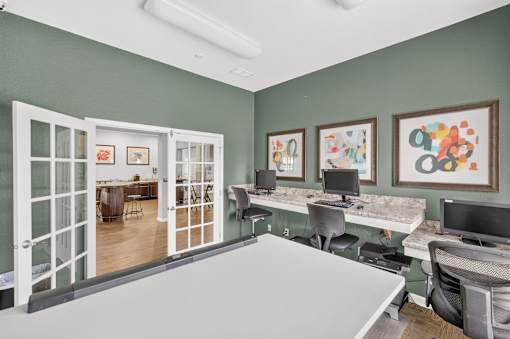 A room with a white desk and chairs, a white computer desk with two monitors, and a white framed picture on the wall.