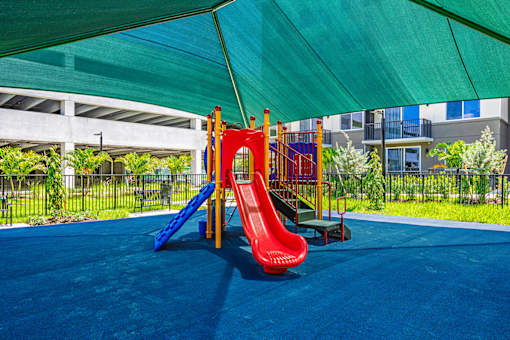 A playground with a red slide and a blue slide under a green canopy.