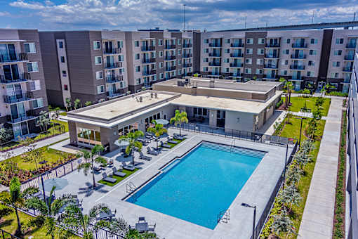 A large swimming pool is surrounded by a concrete patio and lounge chairs.