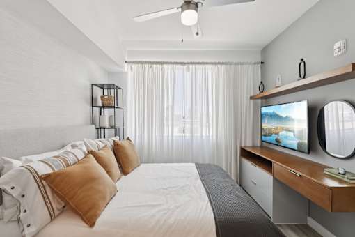 A bedroom with a bed, a television, and a ceiling fan.