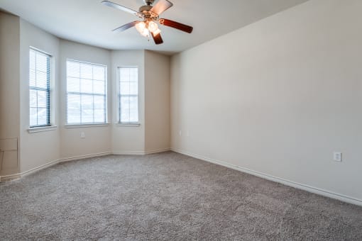 an empty room with a ceiling fan and three windows