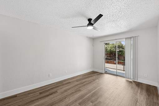 A room with a ceiling fan and sliding glass doors leading to a balcony.