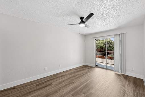 A room with a ceiling fan and sliding glass doors leading to a balcony.