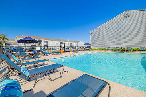 A pool with sun loungers and a building in the background.