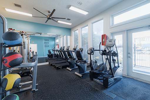 A gym with a variety of equipment including treadmills, weights, and a fan.