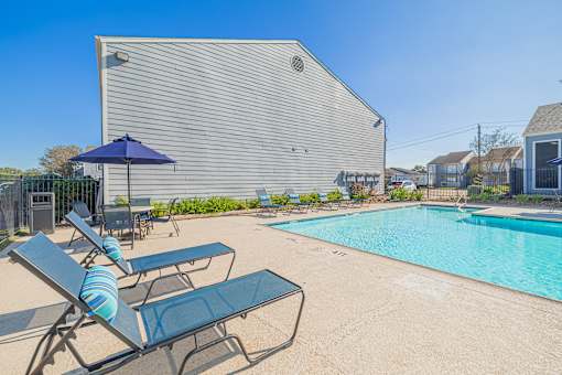 A pool area with lounge chairs and umbrellas in front of a building.