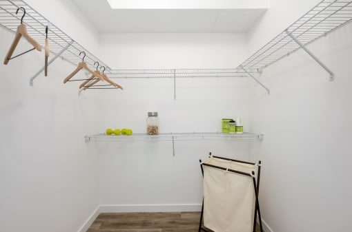 room with white walls and a white closet with hanging racks and a shelf with towels
