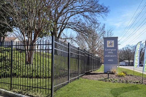 A sign for Covington Apartments stands in front of a black fence.