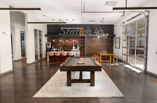 A pool table is in the middle of a room with a bar in the background.