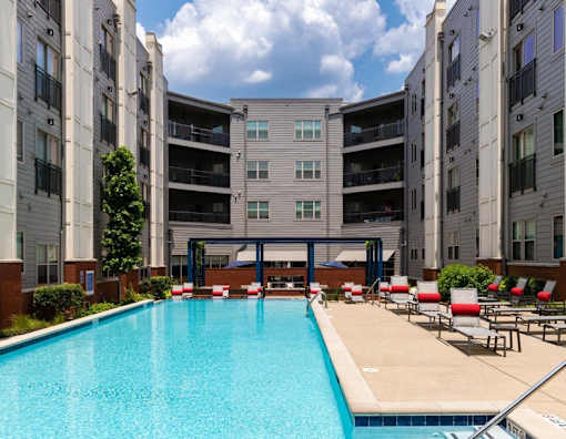 A swimming pool in front of a building with red lounge chairs.