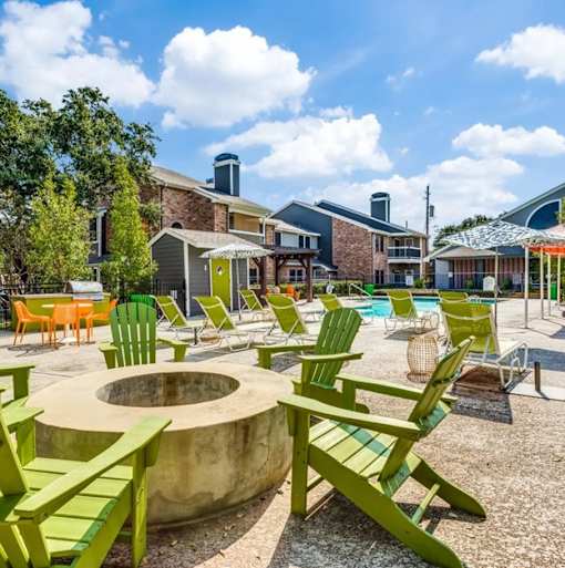 A sunny day at a poolside with green chairs and a fire pit.