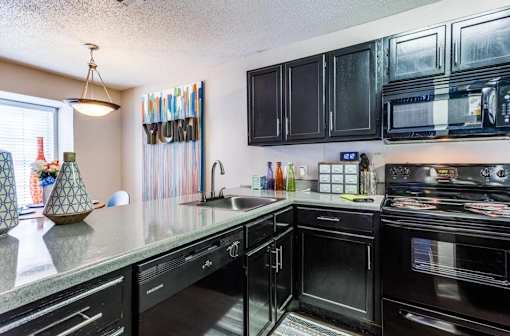 A kitchen with black cabinets and appliances, a window with blinds, and a hanging light fixture.