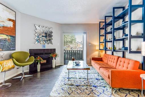 A living room with a fireplace, orange couch, and a painting on the wall.