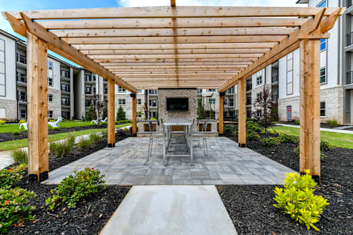 A wooden pergola is over a table set for four in a courtyard.