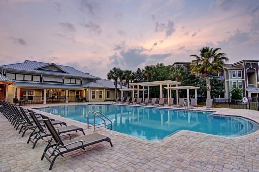 A large swimming pool surrounded by lounge chairs and a building in the background.