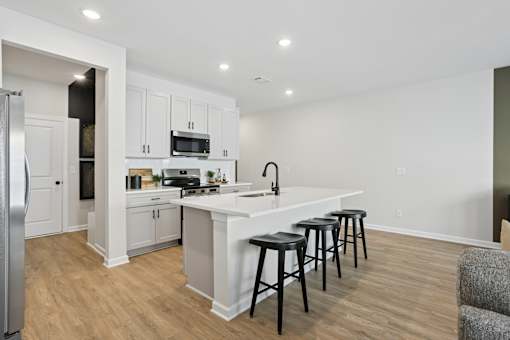 A kitchen with white cabinets and a white island with black stools.