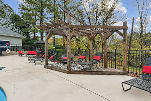 A wooden pergola with red cushioned chairs and a black metal fence.