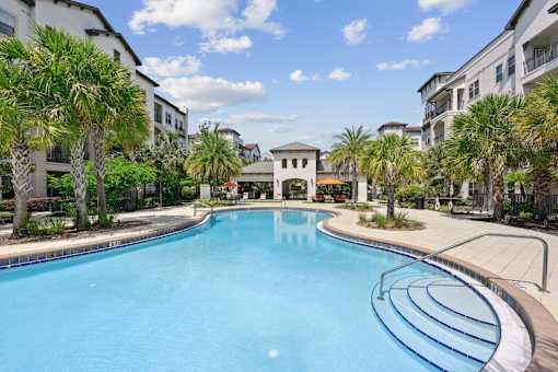 A large swimming pool surrounded by palm trees and buildings.