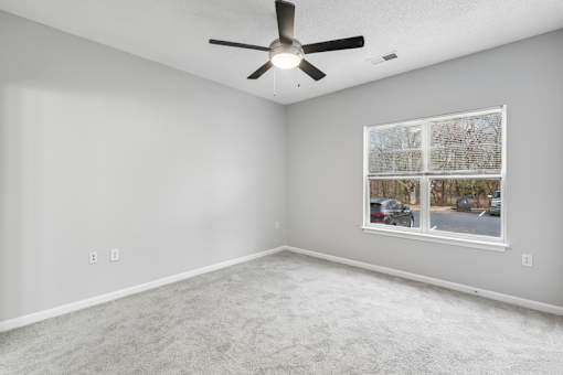 A room with a ceiling fan and a window showing a parking lot outside.