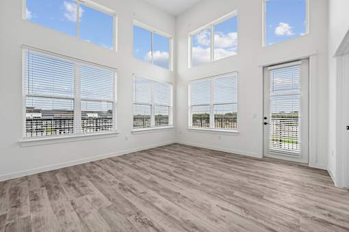 A room with wooden floors and large windows with blinds.