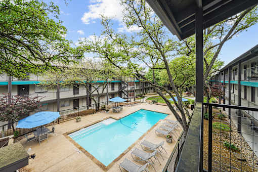 A pool surrounded by trees and chairs.