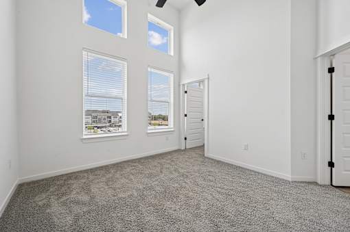 A room with a carpeted floor, two windows with blinds, and a ceiling fan.