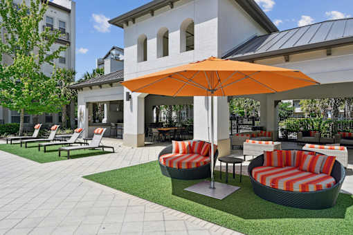 A patio with a striped couch and an orange umbrella.