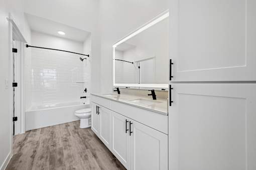A white bathroom with a wooden floor and a large mirror.
