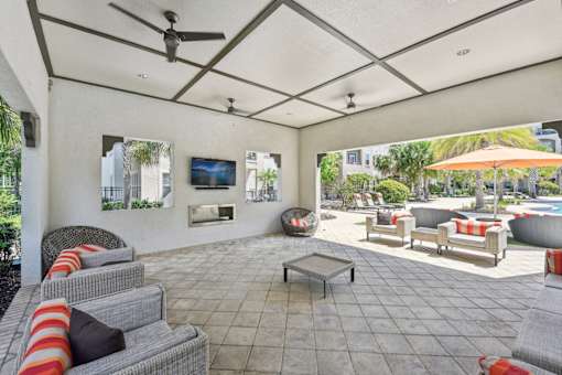A patio with a grey couch and a television on the wall.
