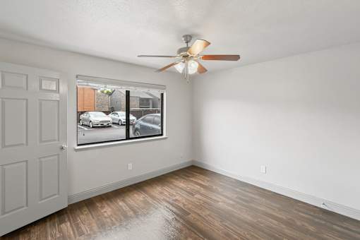 A room with a ceiling fan and a window showing a parking lot outside.