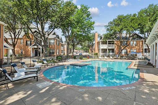 A swimming pool surrounded by trees and chairs in a residential area.