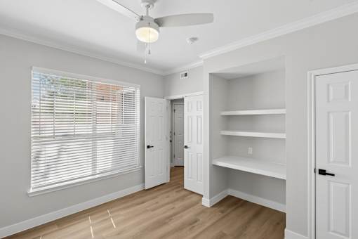 A room with a ceiling fan and a window with blinds.
