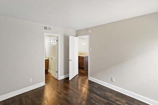 A room with a wooden floor and white walls with two open doors.