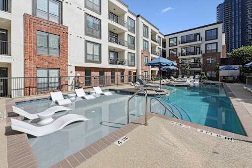 A pool with a slide and sun loungers in front of apartment buildings.