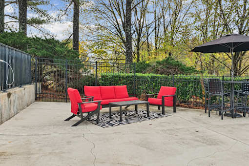 A patio with a red couch and a black umbrella.