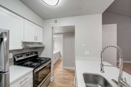 A kitchen with a stove, sink, and cabinets.